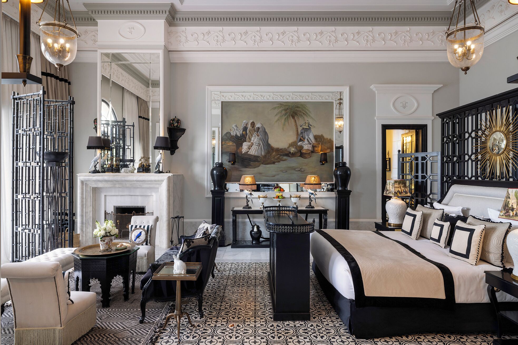 A luxurious bedroom with a large bed, a fireplace, a dining area, and a decorative mirror.
