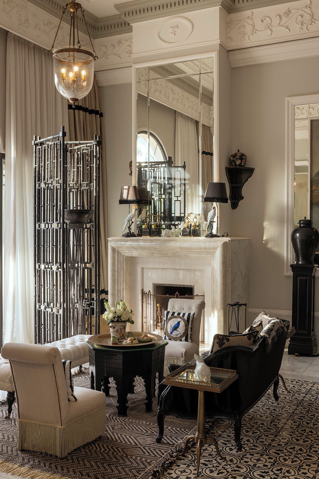 Um quarto com lareira, espelho, candelabro e um biombô decorativo.
