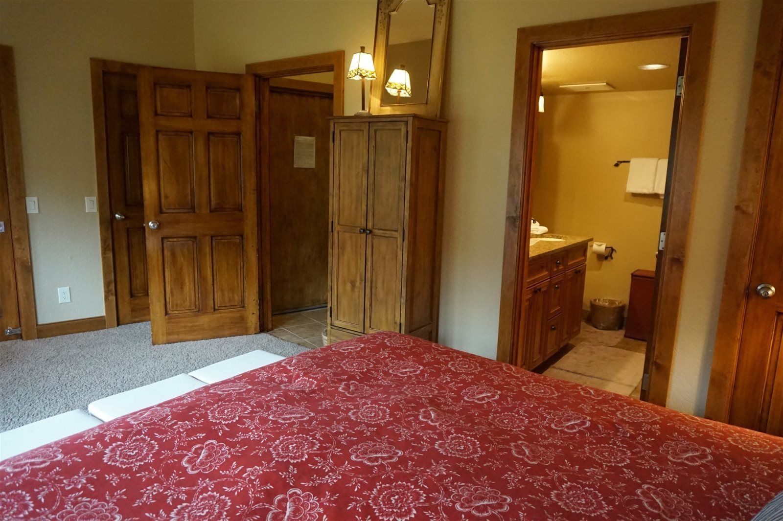 A bedroom with a bed, wooden wardrobe, and a bathroom visible through an open door.