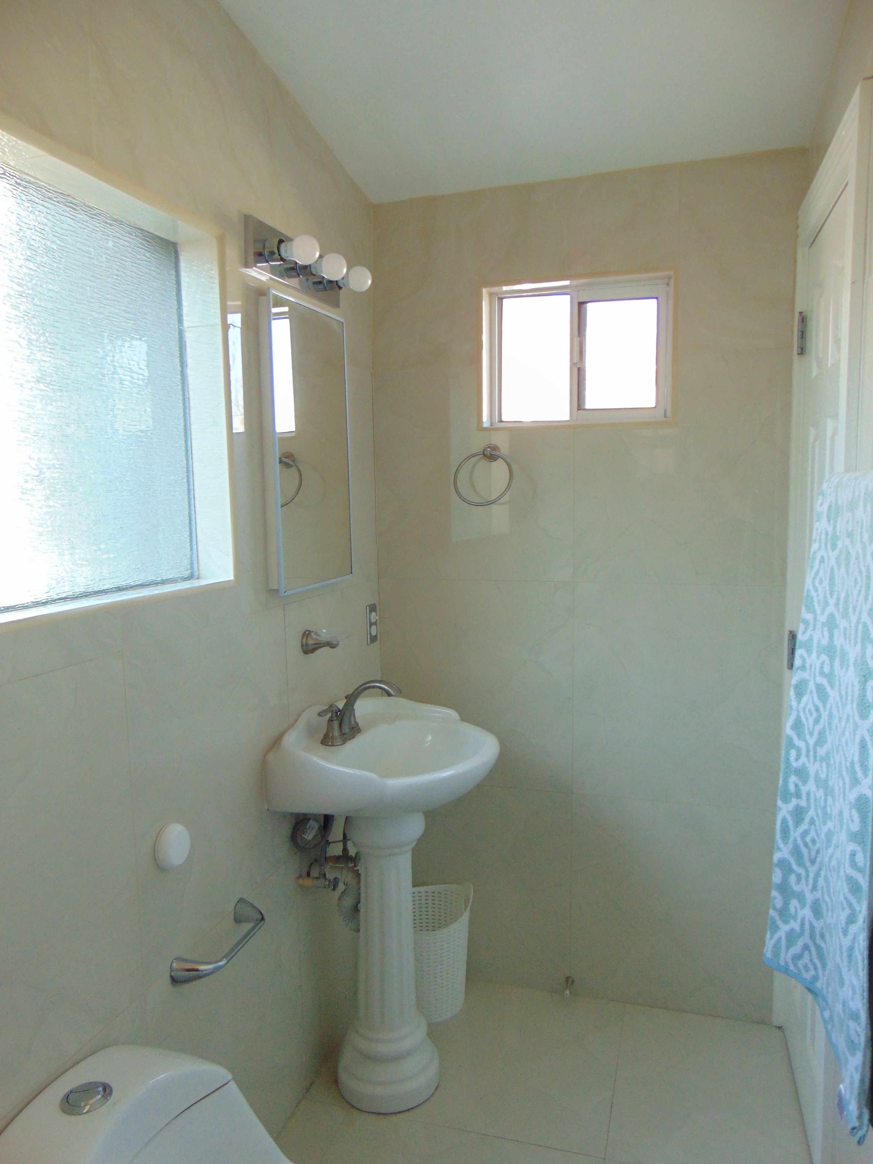 A bathroom with a pedestal sink, a mirror, a window, and a shower curtain.