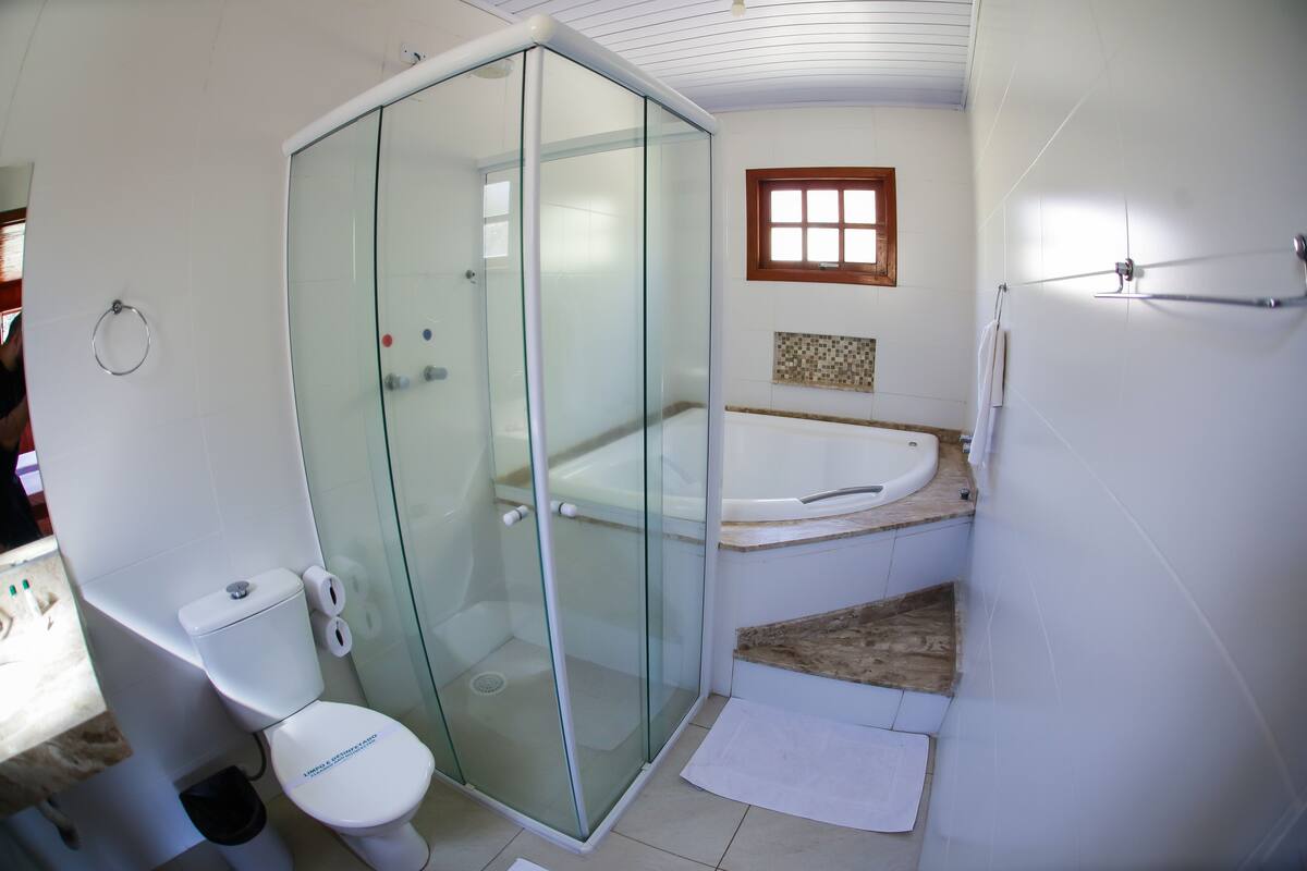 A bathroom with a glass-enclosed shower, a white toilet, a bathtub, and a small window.