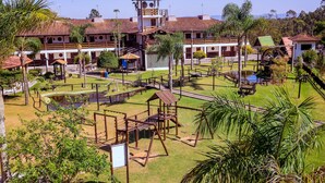 A courtyard with a playground, palm trees, and a building with a water wheel. - Vale Encantado Eco Park & Hotel (Biritiba-Mirim)