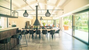 Un comedor amplio con una larga mesa y sillas, una chimenea negra grande y lámparas colgantes.