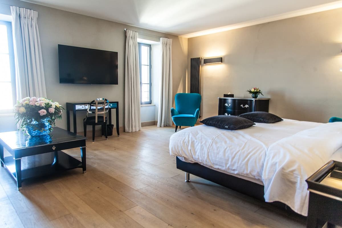 Habitación de hotel con cama, escritorio, silla, televisor y ventana con cortinas.