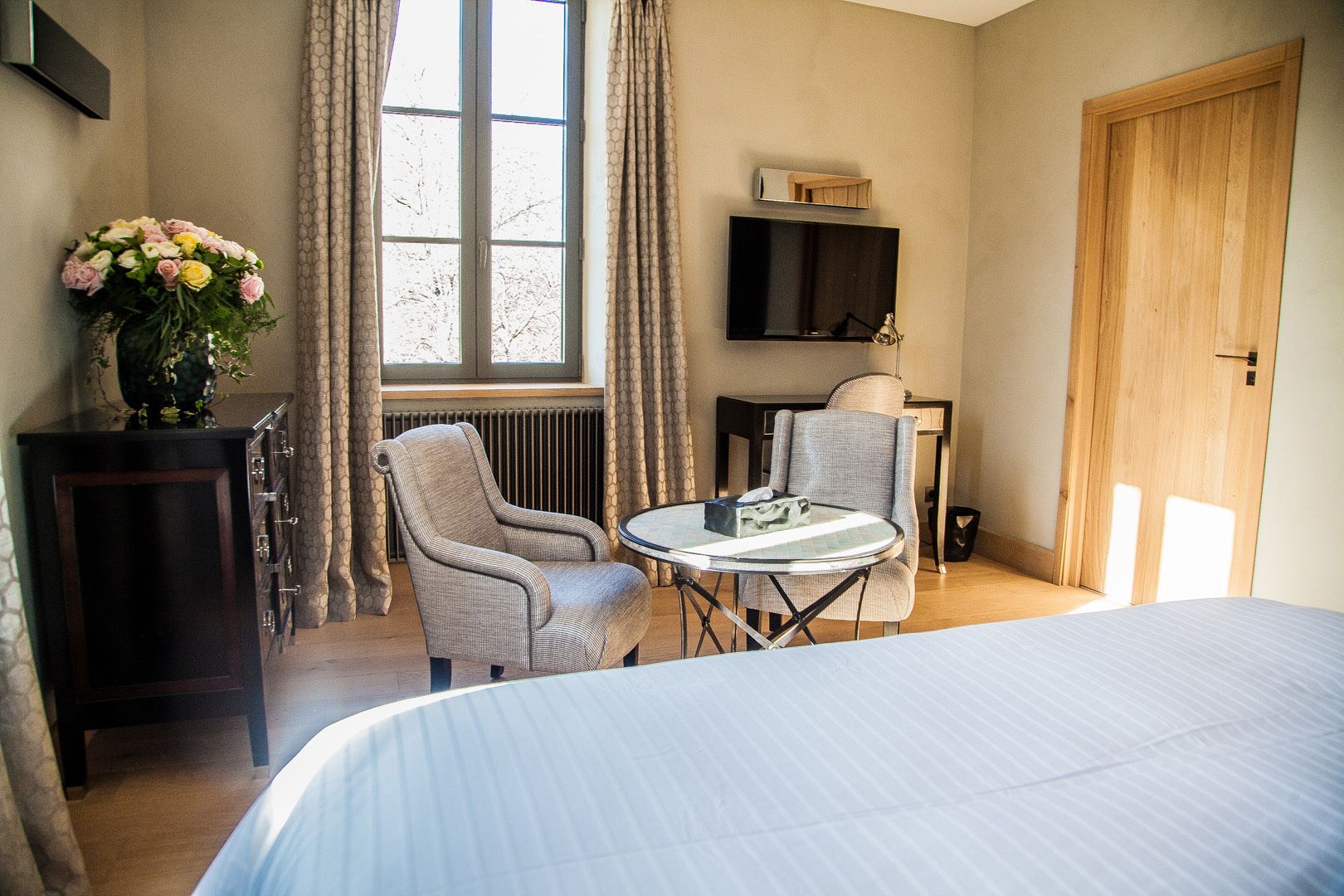 Une chambre d’hôtel avec un lit, un bureau et une chaise, une télévision et une fenêtre avec des rideaux.