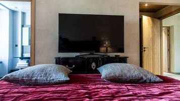 Un dormitorio con una televisión de pantalla plana grande montada en la pared, una cama con una colcha roja y dos almohadas.