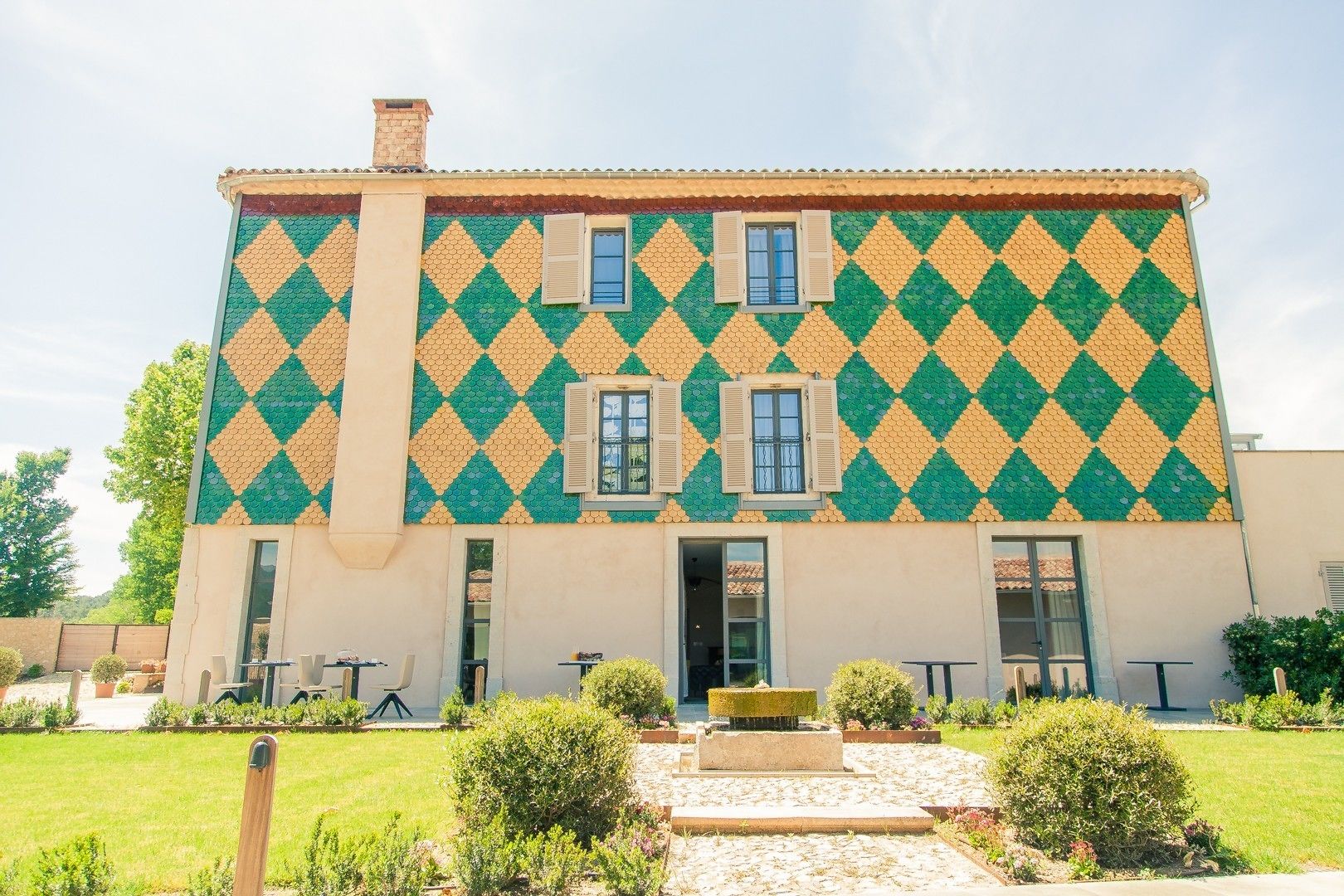 A building with a distinctive diamond-patterned exterior, a central entrance, and a small garden area with seating.