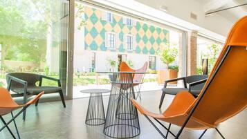 A modern indoor seating area with a glass wall, a patterned exterior wall, and a view of a garden.