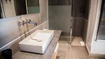 A modern bathroom with a rectangular sink, a mirror, and a shower area.