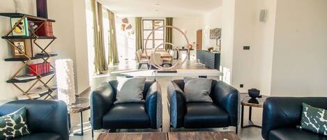 A modern living room with two black leather sofas, a wooden coffee table, and a bookshelf.