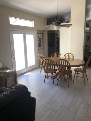 A dining area with a round wooden table and six chairs, a ceiling fan, and a view of the kitchen through an open door.