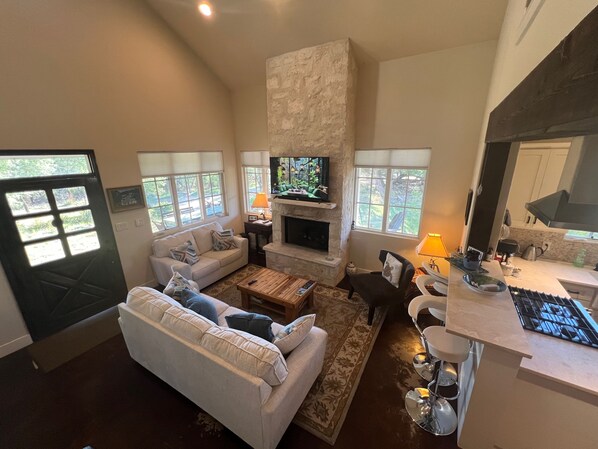 A spacious living room with a fireplace, a television, and a kitchen area with modern appliances. - Heaven in the Hills. Welcome to Monticello Cottage (Dripping Springs)