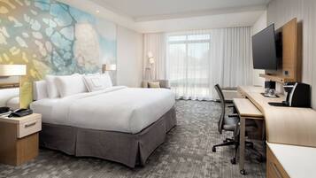 A hotel room with a large bed, a desk, a flat-screen TV, a lamp, and a painting on the wall.