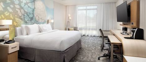 A hotel room with a large bed, a desk, a flat-screen TV, a lamp, and a painting on the wall.