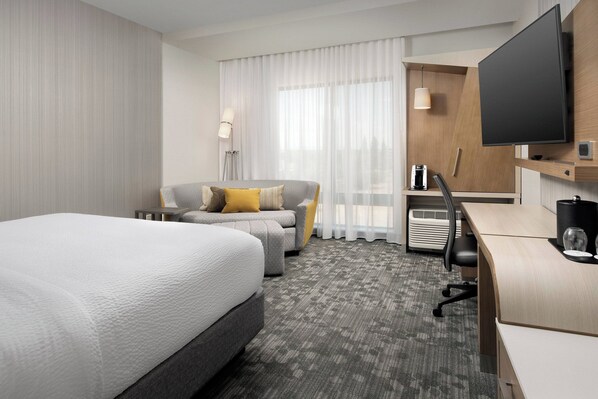 A hotel room with a large bed, a sofa, a desk, a television, and a window with curtains.