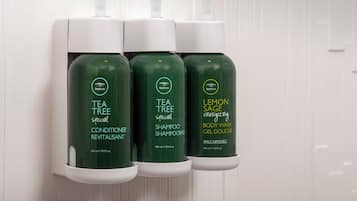 Three bottles of Tea Tree shampoo and conditioner, and a bottle of Lemon Sage body wash, all in a white dispenser.
