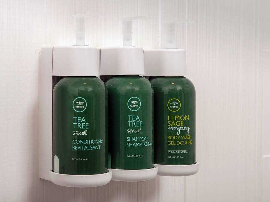 Three bottles of Tea Tree shampoo and conditioner, and a bottle of Lemon Sage body wash, all in a white dispenser.