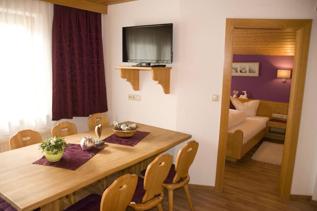 Un coin repas avec une table en bois, des chaises et un téléviseur fixé sur une étagère en bois.