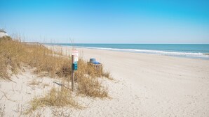 Een strand met een waarschuwingsbord en een vuilnisbak.