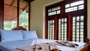 A bed with a wooden headboard, a window with a grid pattern, and a view of greenery outside.