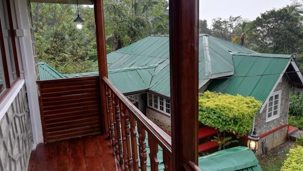 A wooden balcony with a view of a house with a green roof and stone walls.