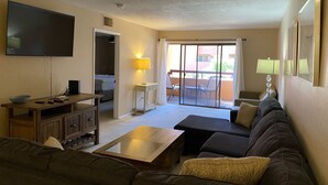 A living room with a sofa, coffee table, TV, and a sliding glass door leading to an outdoor area with chairs. - Summer tenant special, 1 BR Condo with sparkling pool view!  RELAXATION IN AZ! (Phoenix)