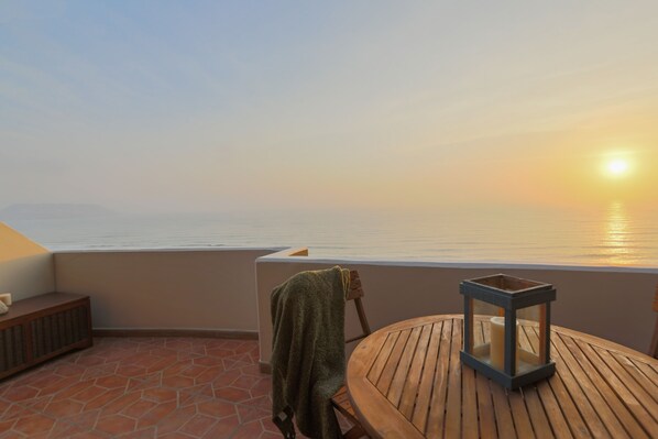 A wooden table with a lantern on a balcony overlooking a body of water during sunset.