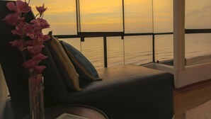 Ein Zimmer mit großem Fenster mit Blick aufs Meer, ein dunkelbraunes Sofa und eine Vase mit rosa Blumen.