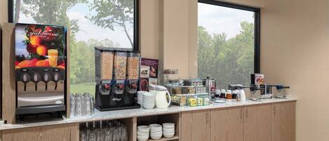 Una barra de desayuno con dispensador de jugo, cereales y diversas opciones de alimentos.