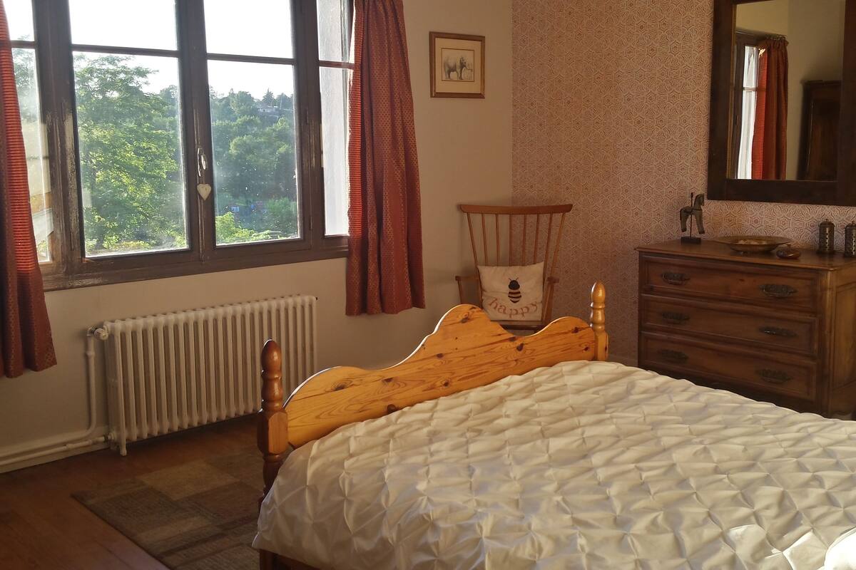 Um quarto com uma cama de madeira, uma cômoda, um radiador e uma janela com cortinas.