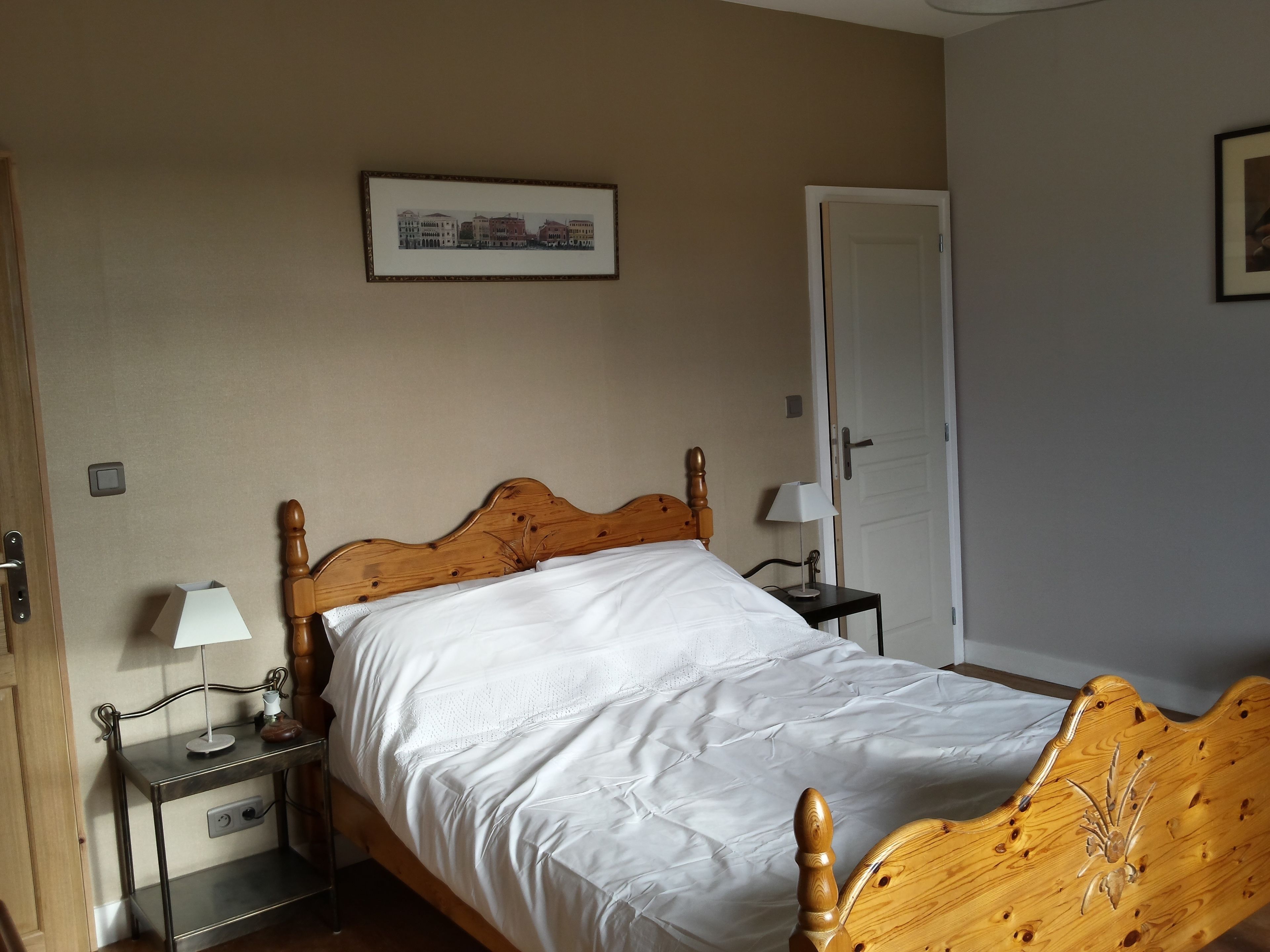 Una cama bien hecha con cabecera de madera, una mesita de noche con lámpara y un cuadro enmarcado en la pared.