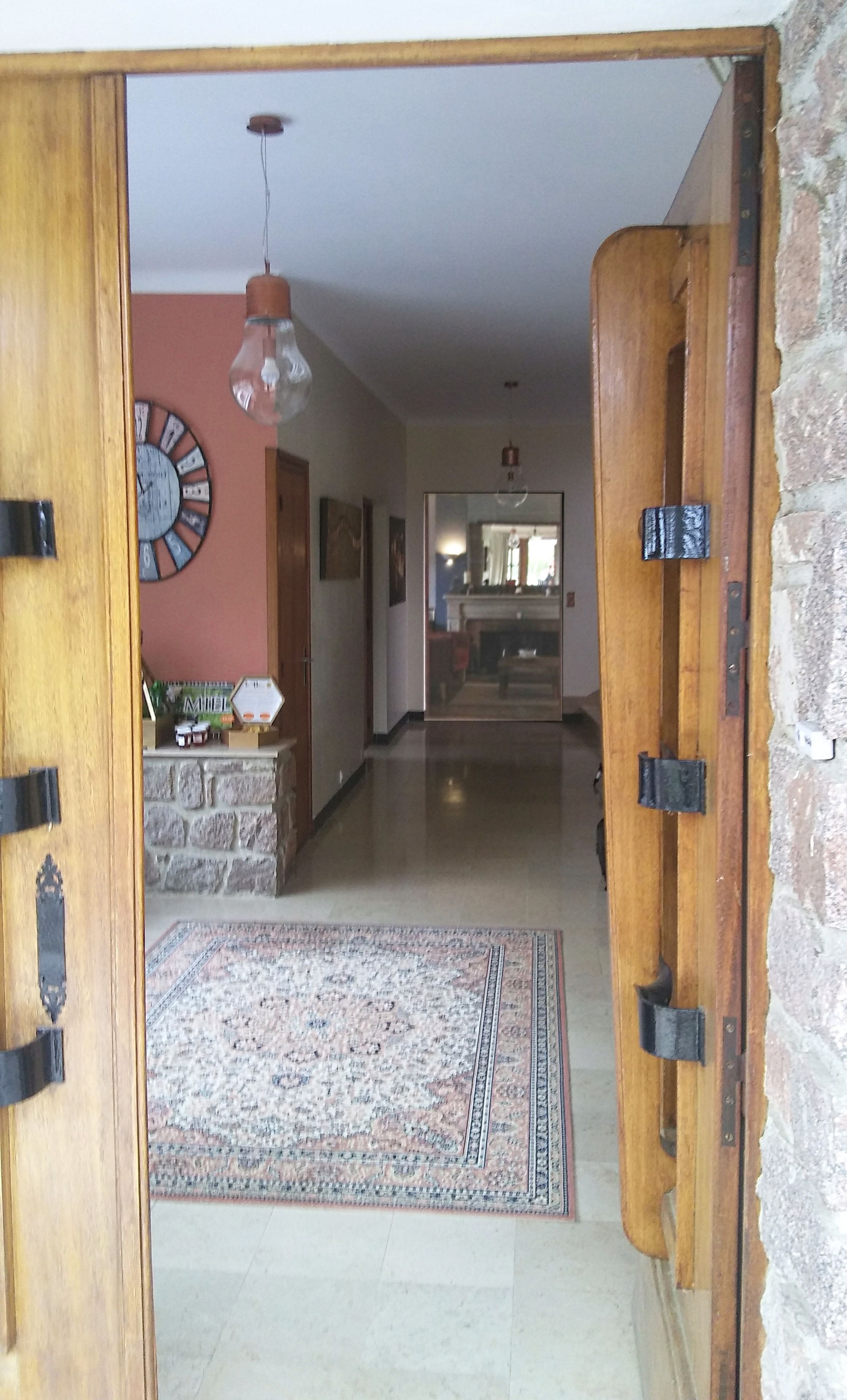 Un couloir avec une porte en bois, un tapis, une horloge et un mur en pierre.