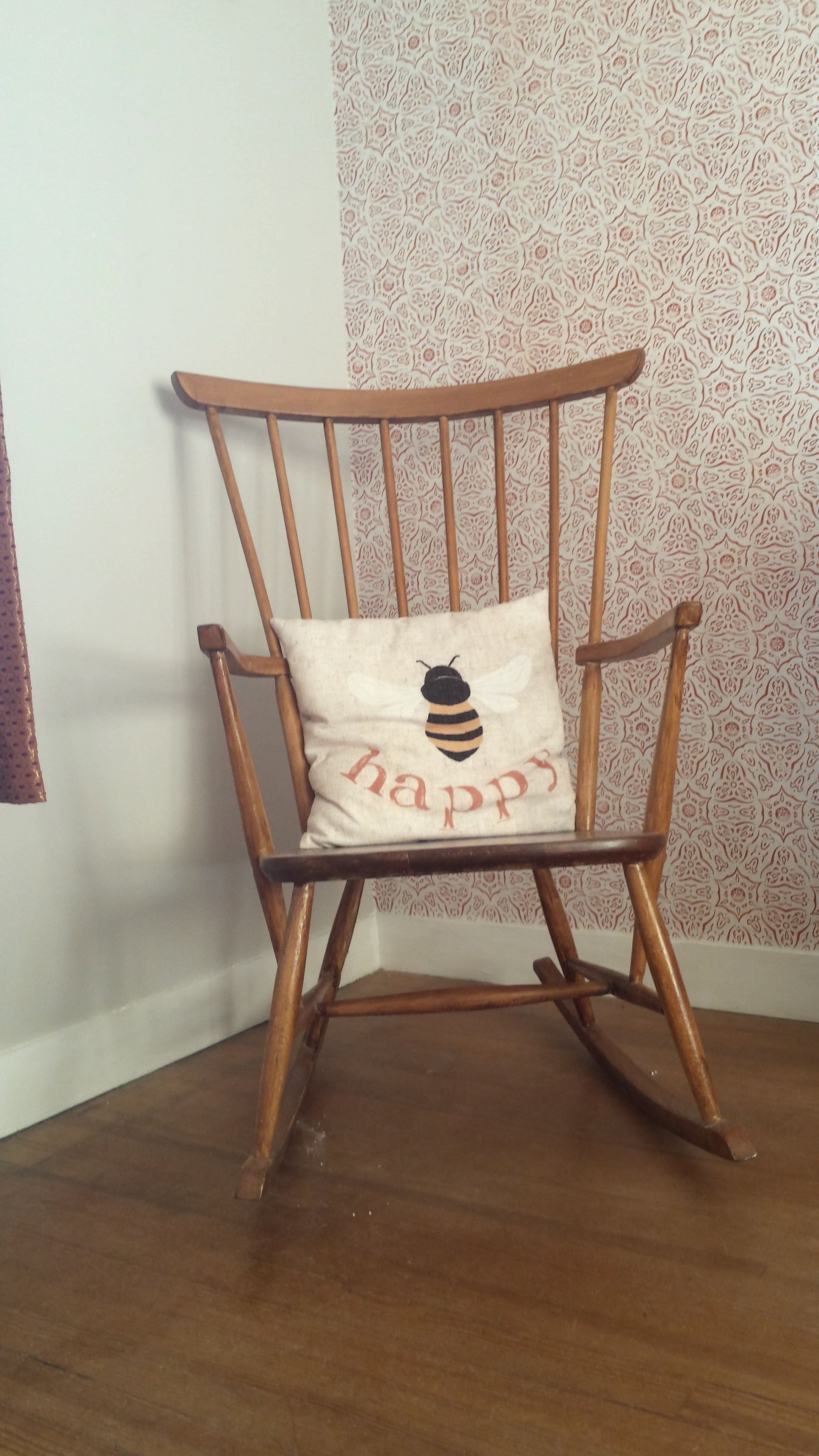 A wooden rocking chair with a cushion featuring a bee and the word "happy".
