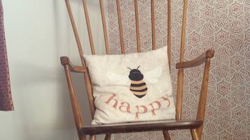 A wooden rocking chair with a cushion featuring a bee and the word "happy".