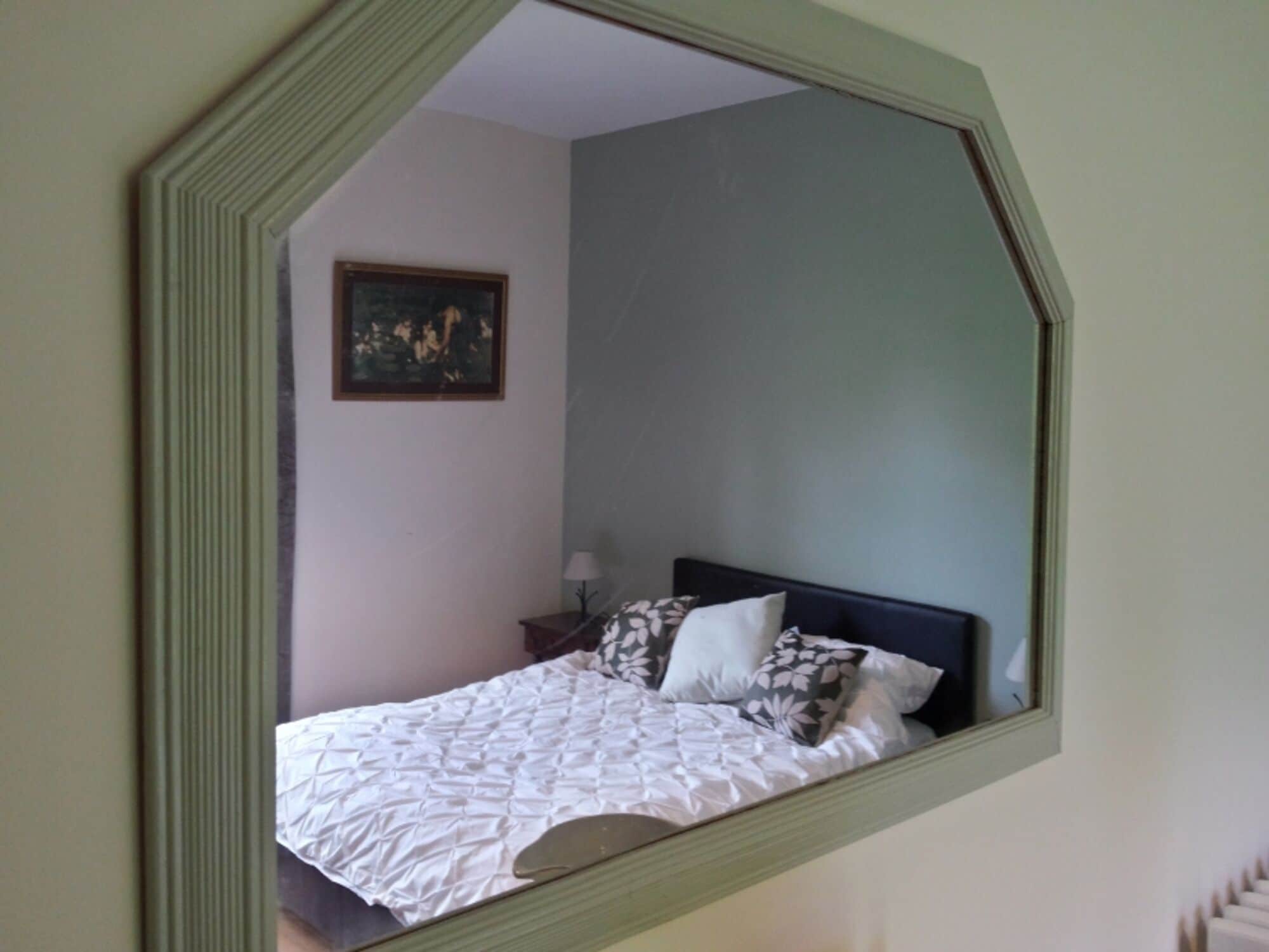Un dormitorio con cama, mesita de noche, lámpara y un cuadro en la pared.