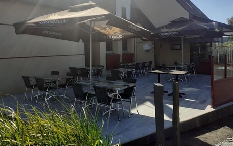 An outdoor seating area with tables and chairs, shaded by umbrellas with 'GRIMBERGEN' branding, and a building with a sloped roof in the background.
