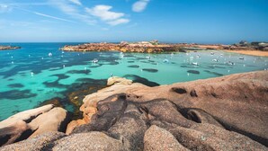 A coastal landscape with clear turquoise waters, rocky formations, and boats anchored in the bay. - Hôtel Le Goas Plat (Paimpol)