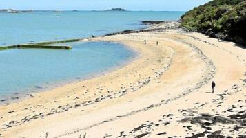 A beach with clear water, a curved shoreline, and rocky outcrops.
