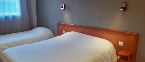 Ein Hotelzimmer mit zwei Betten, einem Nachttisch, einer Wandleuchte und einem Fenster mit Vorhängen.