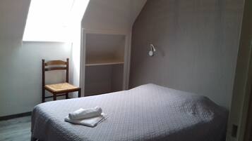 Une petite pièce faiblement éclairée, avec un lit simple, une chaise en bois et une armoire.