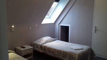 Una habitación pequeña y tenuemente iluminada con una cama individual, una mesita de noche, una puerta y un tragaluz.