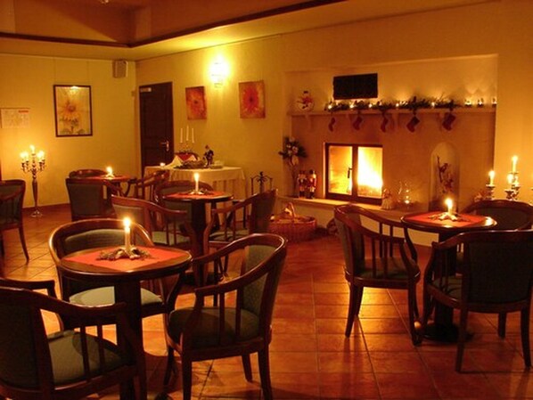 A warmly lit dining area with multiple tables and chairs, a fireplace with stockings, and wall-mounted artwork. - Elbhotel Bad Schandau (Bad Schandau)