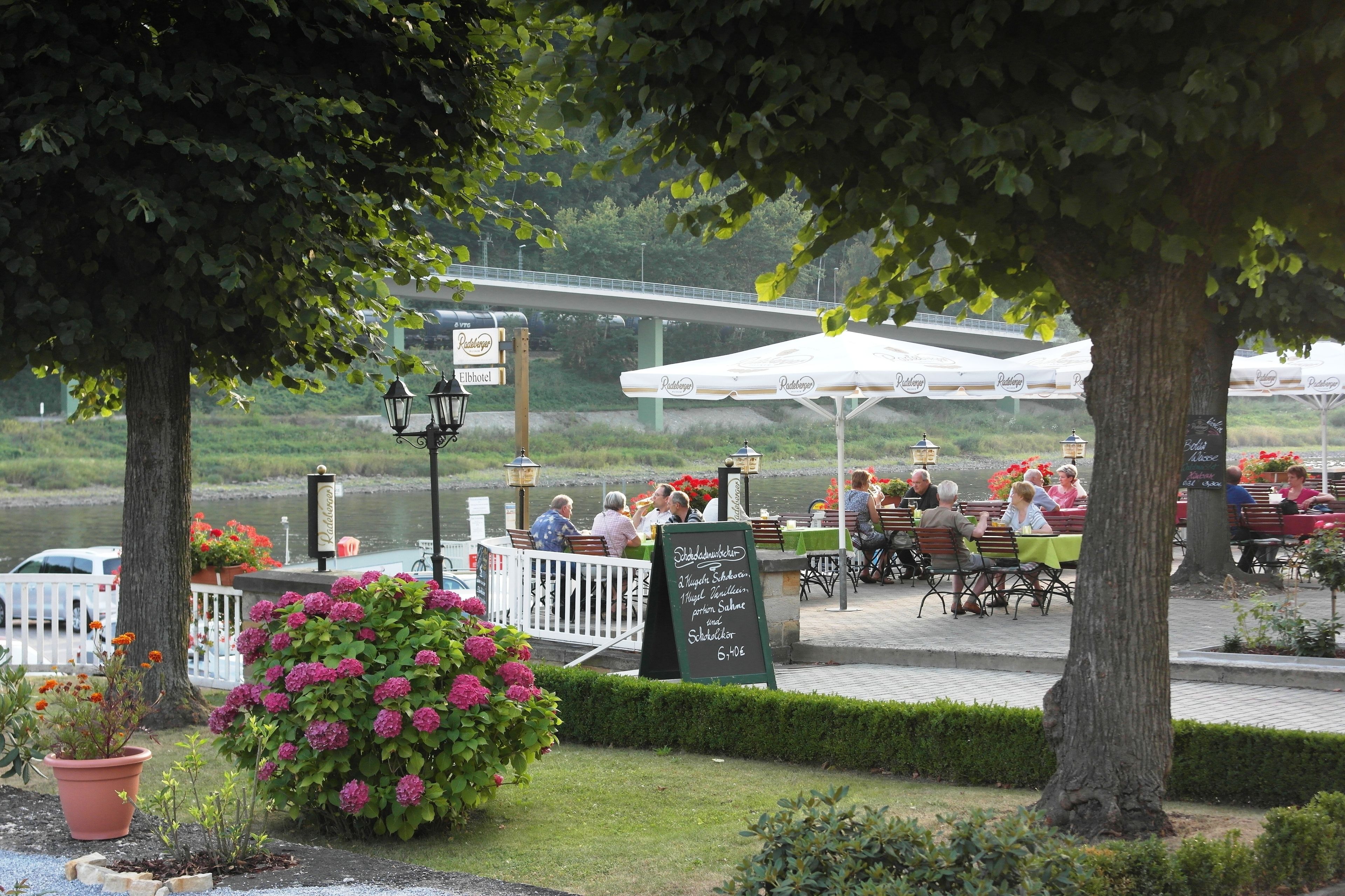 An outdoor restaurant with tables and chairs, a signboard, and a river in the background.