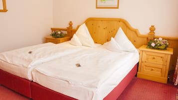 A double bed with white linens, a wooden headboard, and a red accent on the bed frame. There are two bedside tables with lamps and a small bouquet of flowers on one.