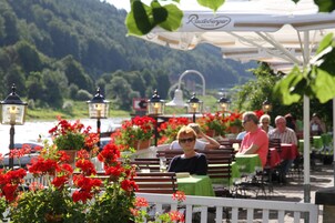 An outdoor seating area with tables and benches, surrounded by red flowers and greenery, with a mountainous backdrop.