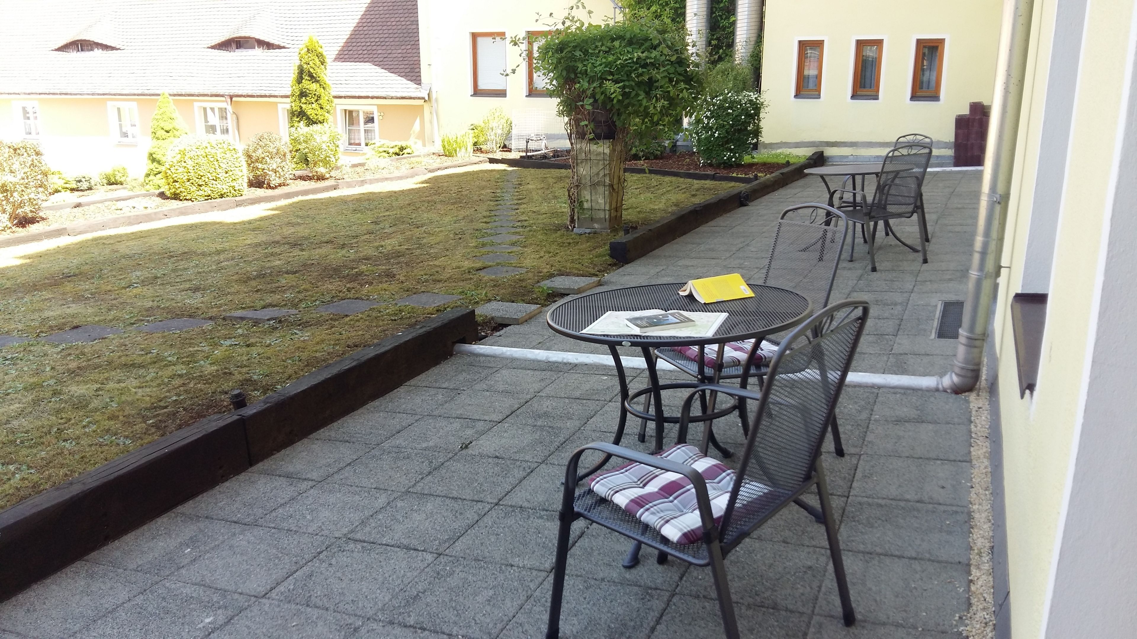 Un patio con una mesa y sillas, un jardín pequeño y un edificio al fondo.