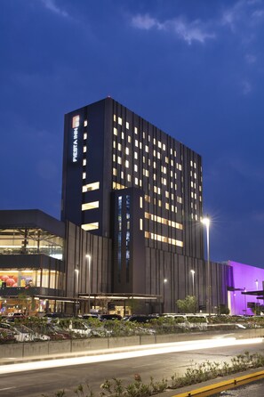 A modern hotel with a prominent 'Fiesta Inn' sign, a large parking area, and a well-lit facade.