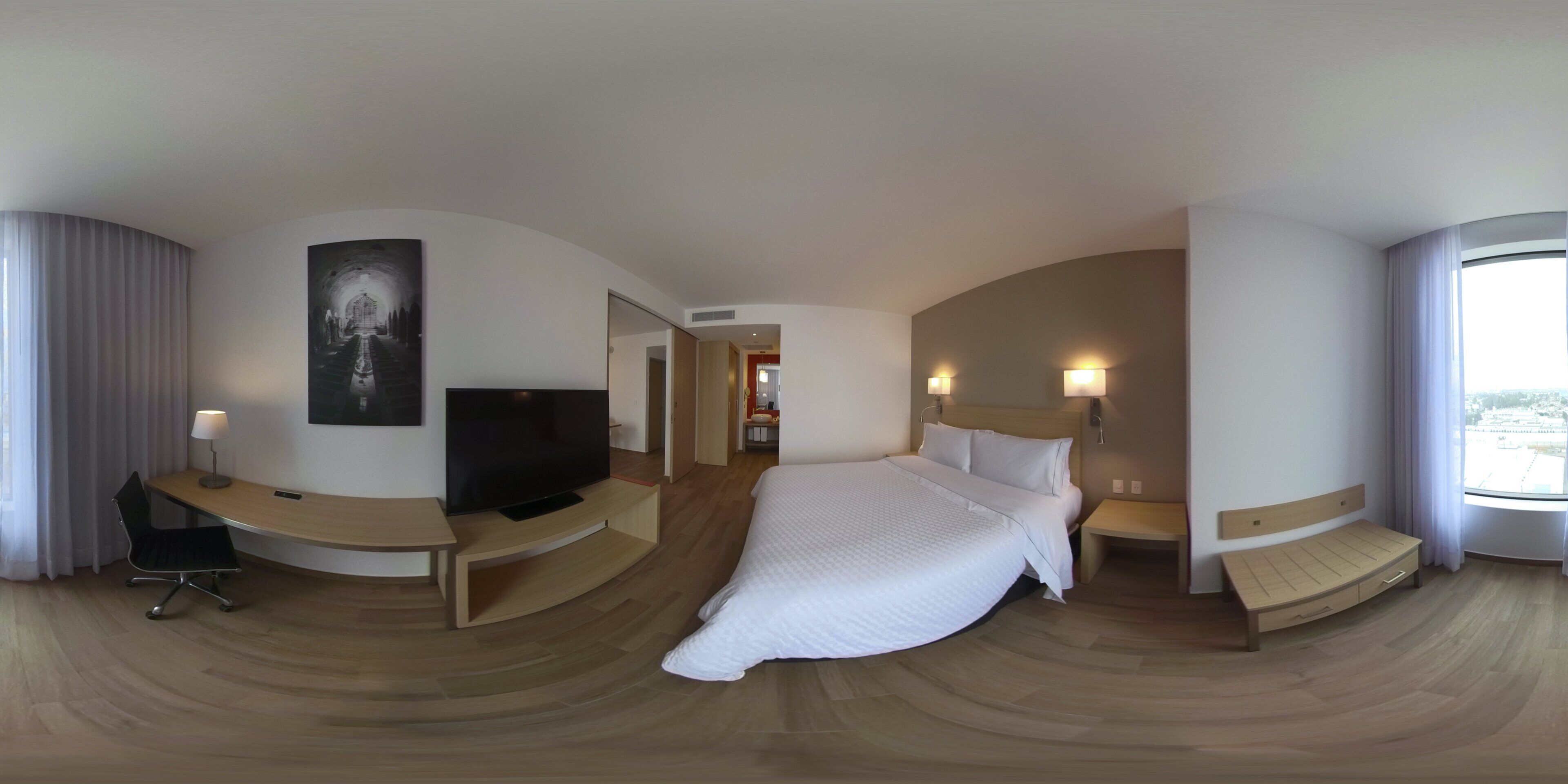 Een moderne hotelkamer met een groot bed, een bureau met een televisie en uitzicht op de stad.