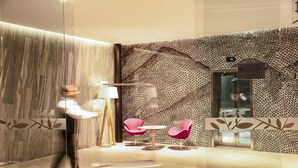A modern interior with a patterned wall, a glass partition, and a seating area with two chairs and a table. - Fiesta Inn Parque Puebla (Puebla)