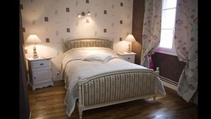 Un dormitorio con cama, dos mesitas de noche, una lámpara de noche, una ventana con cortinas y una pared con estampado floral.
